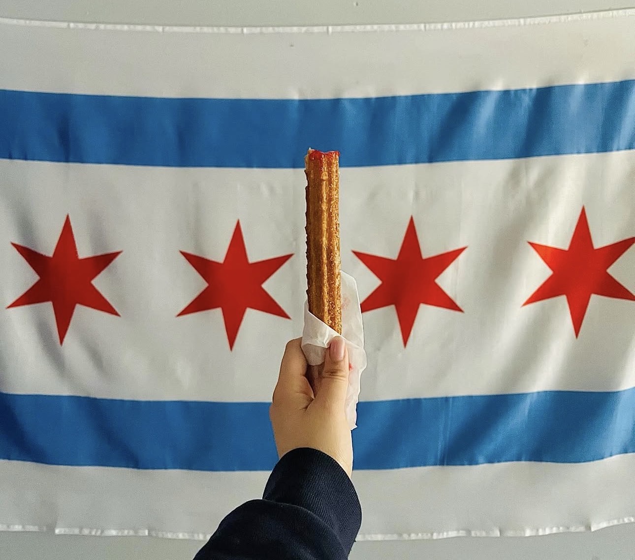 A churro held up proudly in front of the Chicago flag